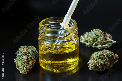 small transparent glass bottle and pipette filled with cannabis oil and dry marijuana flowers around on black background
