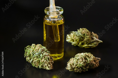 small transparent glass bottle and pipette filled with cannabis oil and dry marijuana flowers around on black background