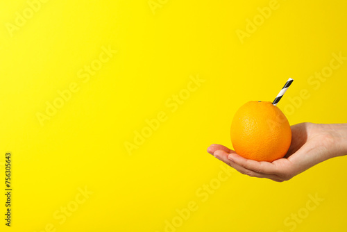 Orange with cocktail straw on hand on yellow background, space for text photo