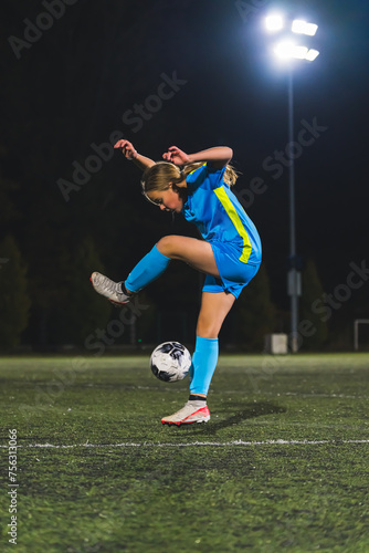 young girl wearing a blue uniform playing with a ball at an evening practice, athlete kids concept. High quality photo