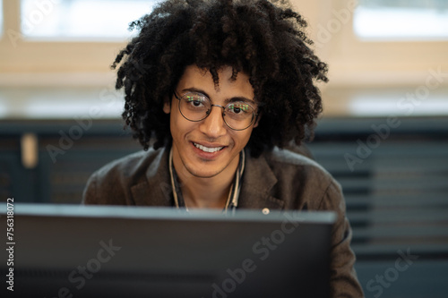 Waist up of a curly-haired young man sitting at computer