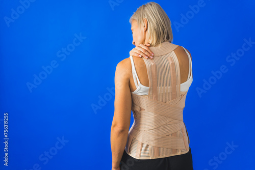 Cuadro en lienzo Young woman in back brace standing over a blue background, woman having back problems