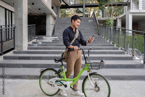 Fototapeta Naklejka Na Ścianę i Meble -  A young Asian businessman rides a bicycle to work. Standing outside the office talking on the phone and talking about business. Concept of reducing energy and reducing air pollution.