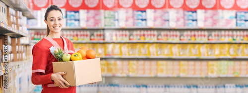 Bild auf Leinwand Smiling supermarket clerk holding a box full of groceries