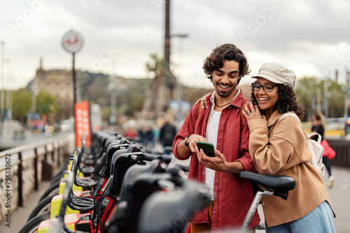 Happy friends pointing at the cellphone and renting a bicycle on city street. © dusanpetkovic1