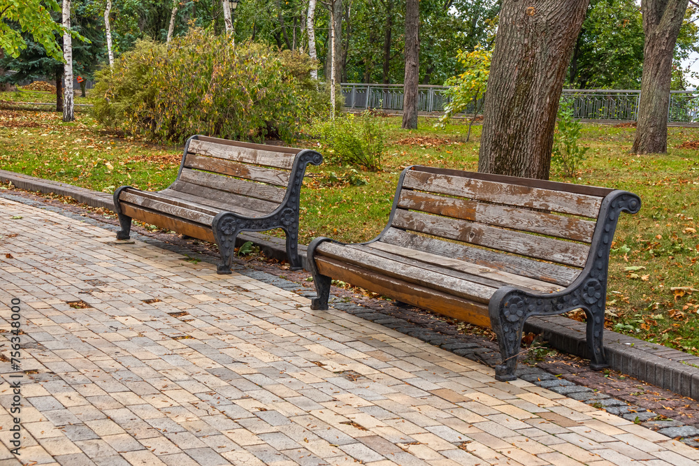 Old wooden benches on an empty alley of a city park Old wooden benches on an empty alley of a city park