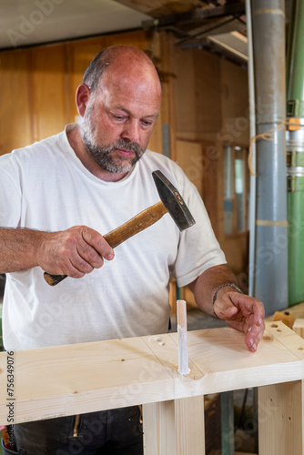 Tischler arbeitet in seiner Werkstatt, schlägt einen Holzdübel ein mit Leim