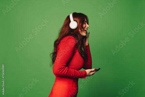 Young woman listening to music with wireless headphones and a smartphone on a green background