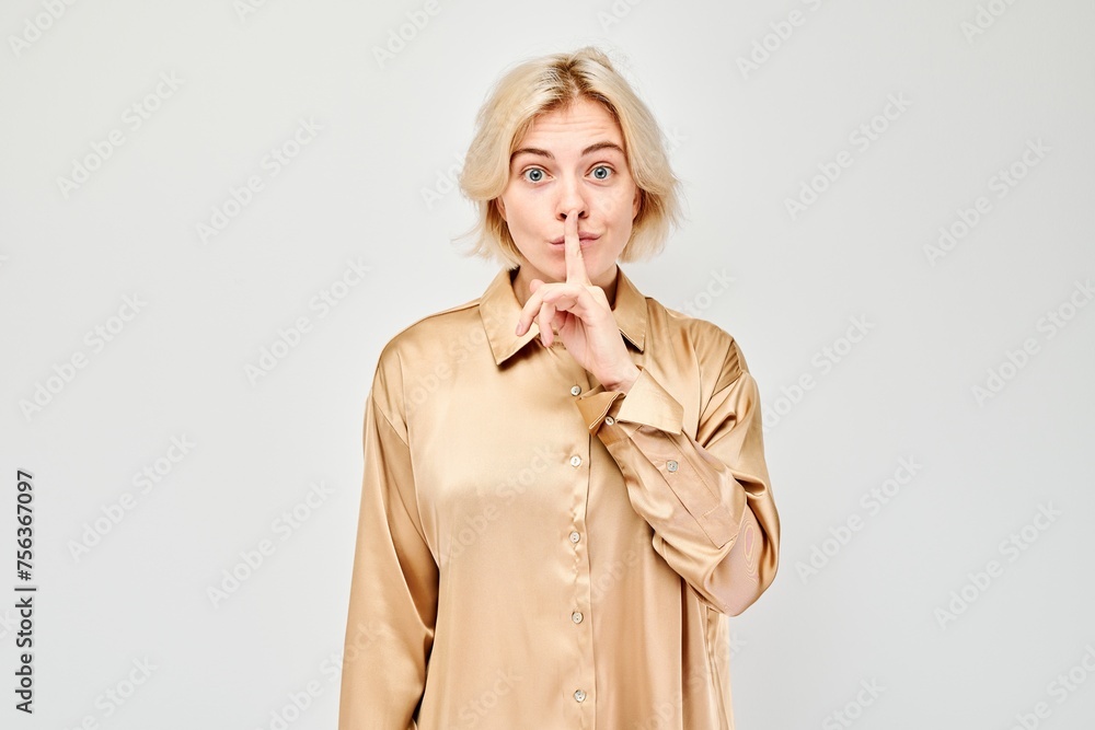 Woman with blonde hair making silence gesture, finger on lips, light background. Woman with blonde hair making silence gesture, finger on lips, light background.