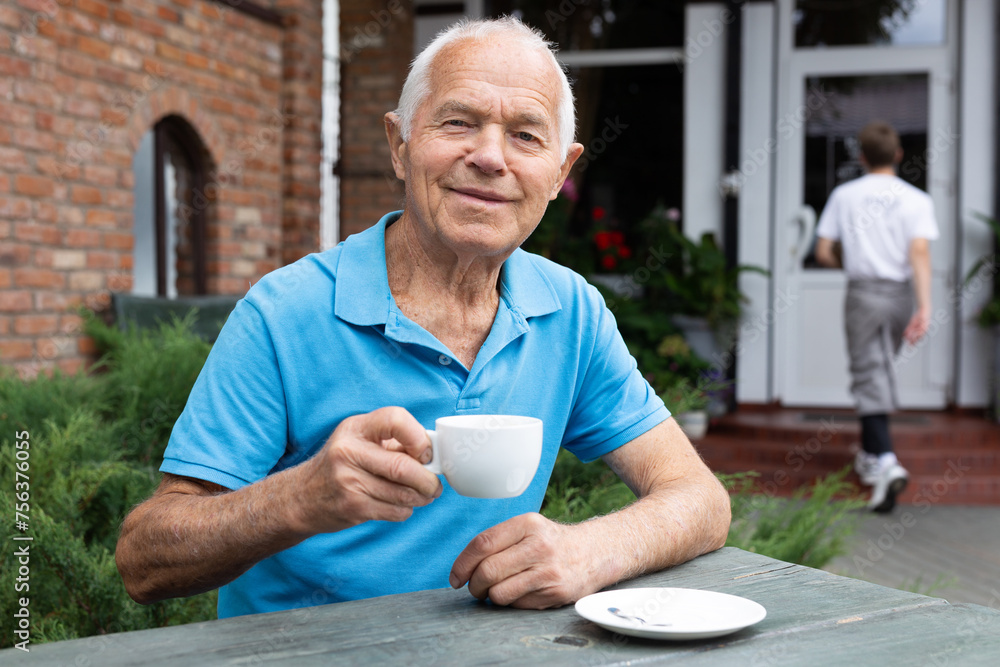Old man sitting at table in outdoor cafe and drinking tea Old man sitting at table in outdoor cafe and drinking tea