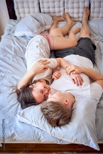 a young couple is lying on the bed, the girl is on the boy's shoulder, tender hugs
