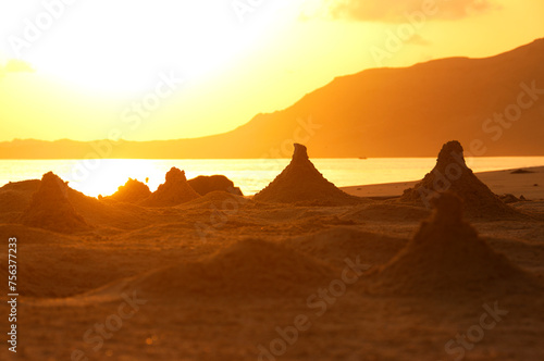 Orange dawn on the ocean shore on a wild beach. Sand pyramids made by crabs on the shore. Calm sea and rocky mountains. 