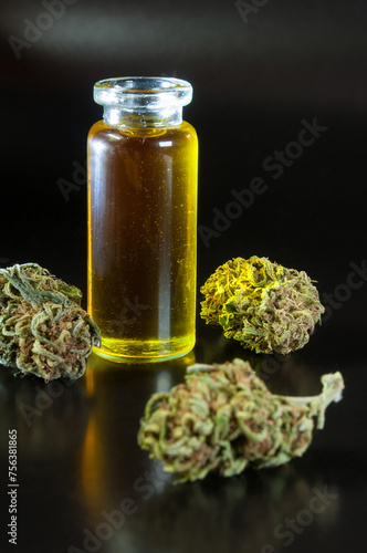 still life of dried marijuana buds and small glass transparent bottle filled with cannabis infused olive oil on black background