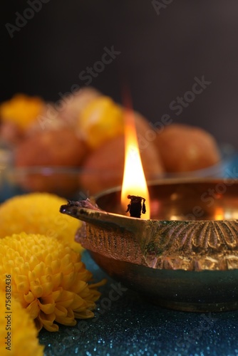 Diwali celebration. Diya lamp and chrysanthemum flowers on shiny light blue table, closeup