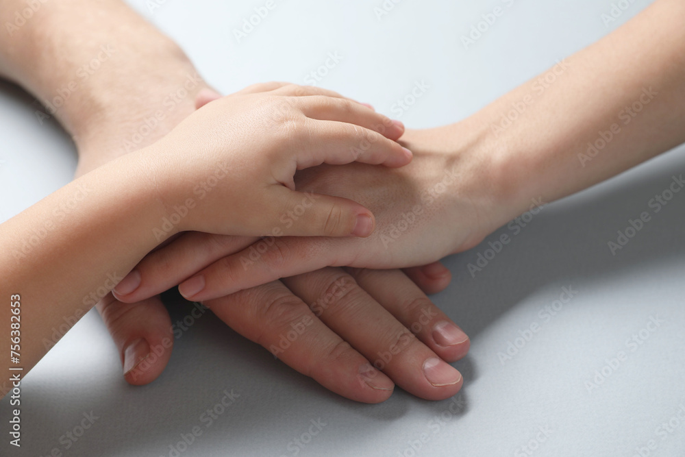 Parents and child holding hands together on gray background, closeup Parents and child holding hands together on gray background, closeup