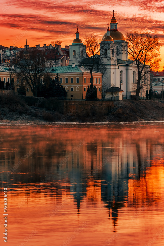 Mirror reflection in the water of the Epiphany Cathedral and the dawn red sky. City of Polotsk, Western Dvina River, Belarus.