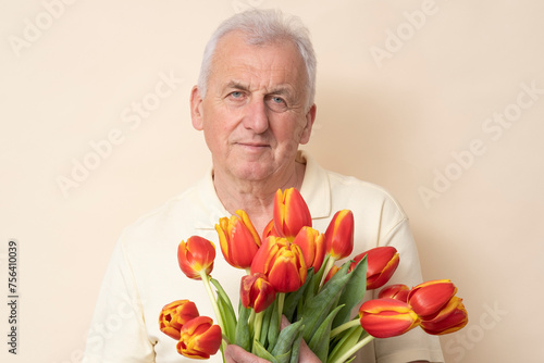 Handsome senior man with a bouquet of tulips on a cream background in the studio.