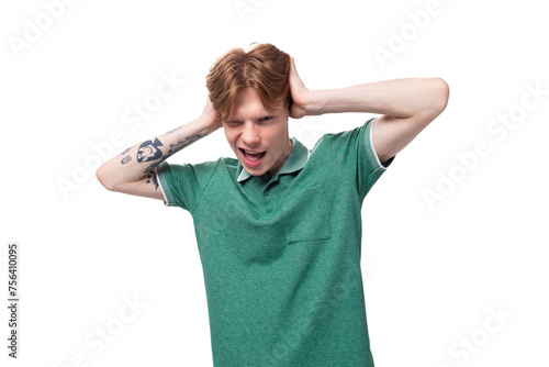 young charming adorable ginger man with a tattoo on his arm dressed in a green short sleeve t-shirt covers his ears with his hands