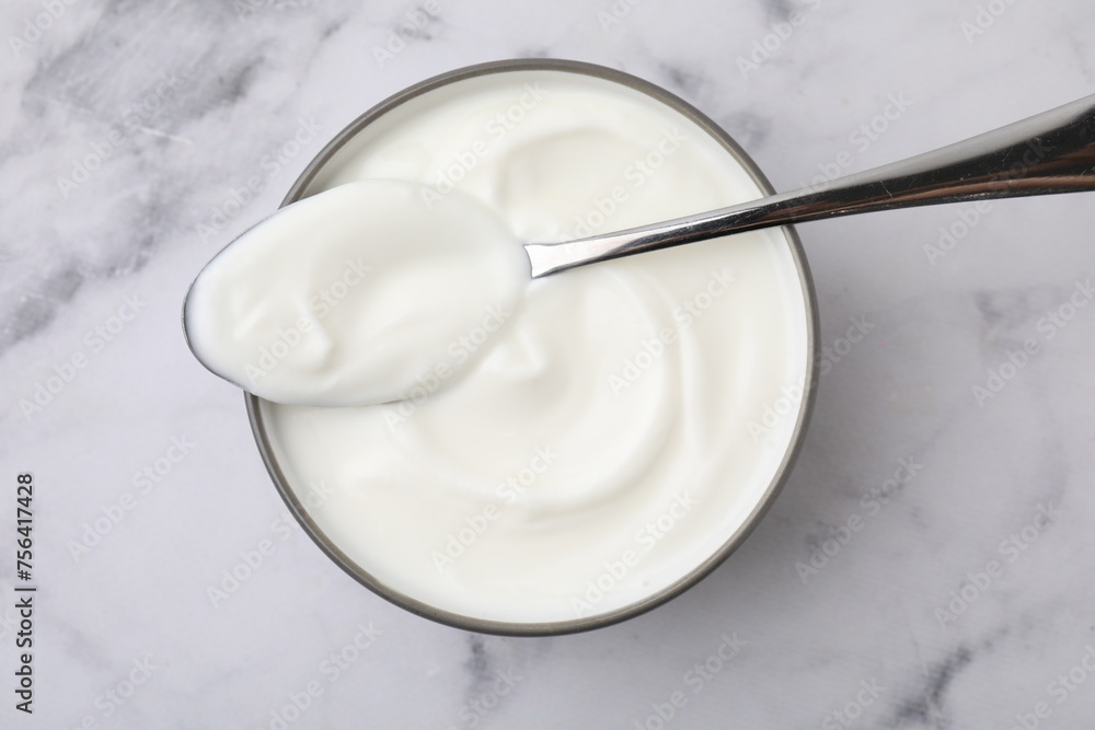 Delicious natural yogurt in bowl and spoon on white marble table, top view Delicious natural yogurt in bowl and spoon on white marble table, top view