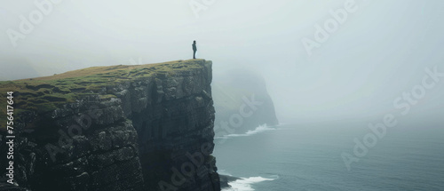 Solitary figure standing on a cliff edge contemplating the vast ocean and misty horizon. photo