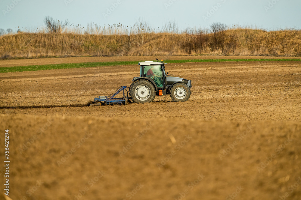 Tractor with a plow attachment works the soil in agricultural farmland during golden hour Tractor with a plow attachment works the soil in agricultural farmland during golden hour