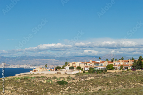 Residential houses on the hillside with a sea view on a seashore. The coast on a sunny day. Townhouses against the blue sky and clouds. Alicante region in Spain