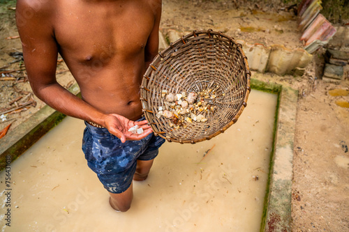 Boy in muddy water hold washed mined gemstone and rattan pan.