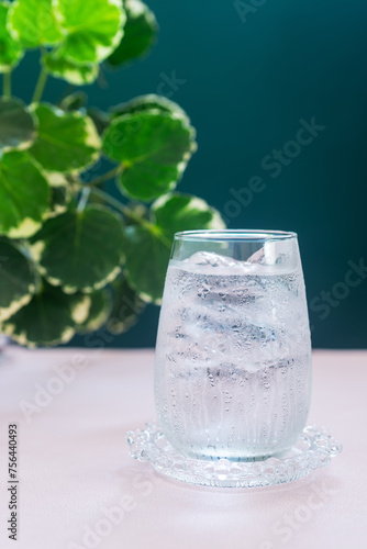 A glass of water with ice on pink table.