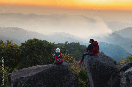 man and a woman are sitting on a rock overlooking a mountain range