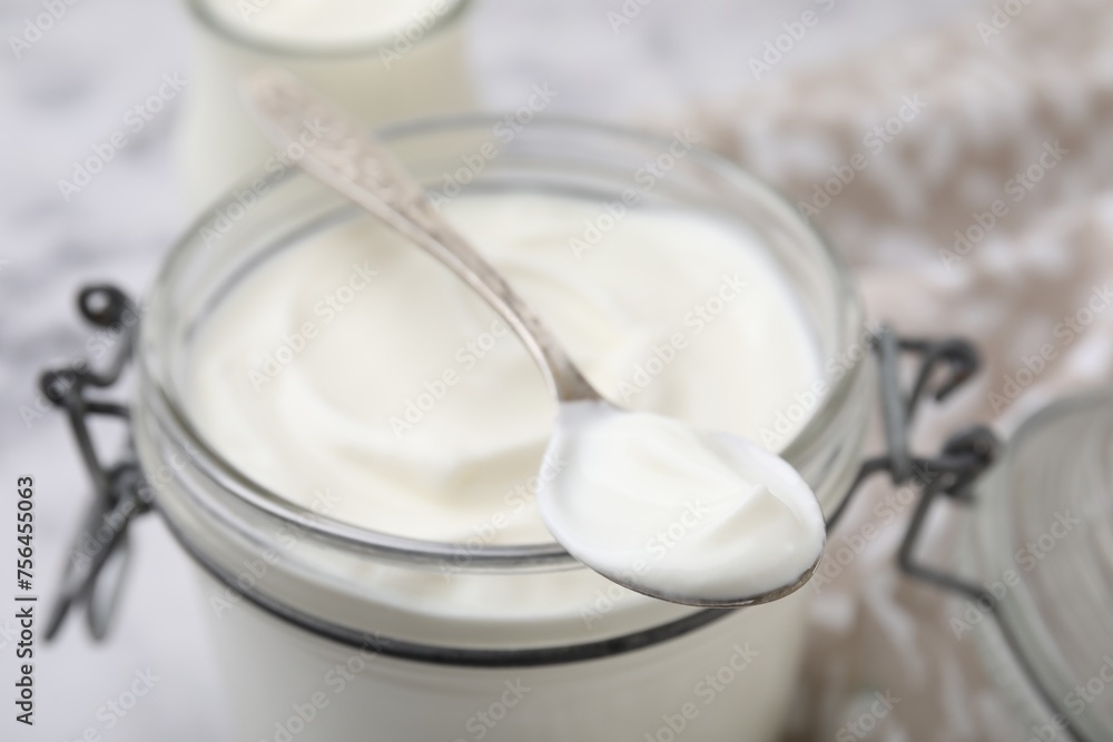 Delicious natural yogurt in glass jar and spoon on table, closeup Delicious natural yogurt in glass jar and spoon on table, closeup