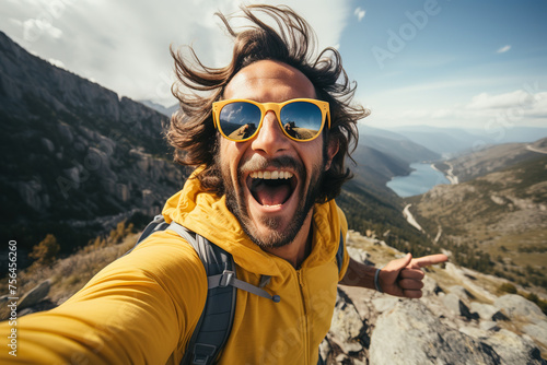 Energetic hiker in yellow jacket takes an exuberant selfie on a mountain peak, with a valley behind