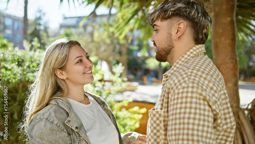 Smiling woman and man lovingly engage in conversation amidst lush green urban park scenery.