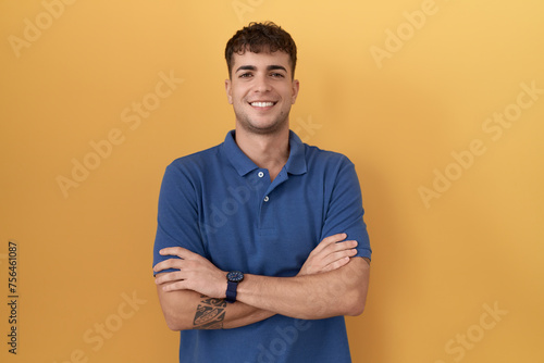 Young hispanic man standing over yellow background happy face smiling with crossed arms looking at the camera. positive person. © Krakenimages.com