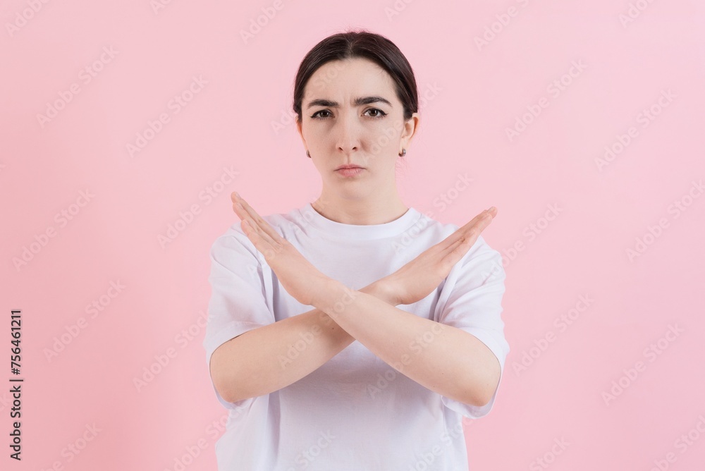 Angry attractive caucasian young brunette woman in casual clothes frowning showing cross hands stop gesture isolated on pink studio background. Angry attractive caucasian young brunette woman in casual clothes frowning showing cross hands stop gesture isolated on pink studio background.