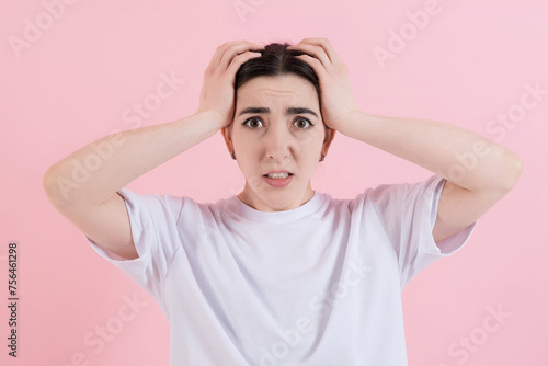 Shocked or stressed attractive caucasian young brunette woman in casual clothing, looking nervously at the camera isolated on a pink studio background.