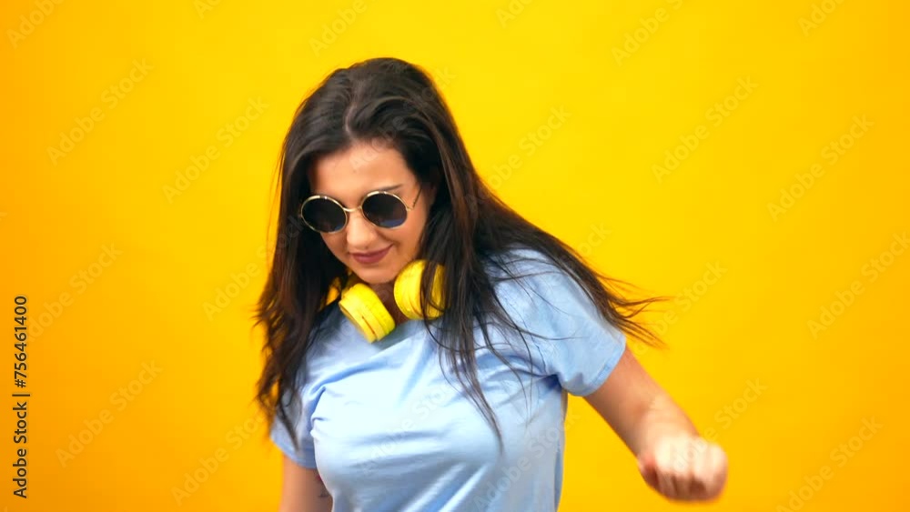Studio portrait with yellow background of a woman waving the hair while using headphones Studio portrait with yellow background of a woman waving the hair while using headphones