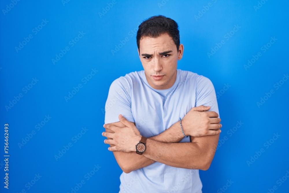 Young hispanic man standing over blue background shaking and freezing for winter cold with sad and shock expression on face Young hispanic man standing over blue background shaking and freezing for winter cold with sad and shock expression on face