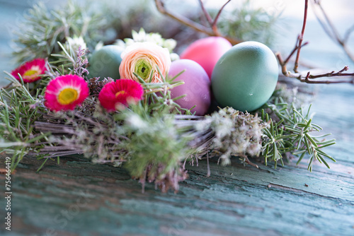 Colorful easter eggs in a herb nest with spring flowers on weathered rustic wooden table. Background with short depth of field. Close-up.