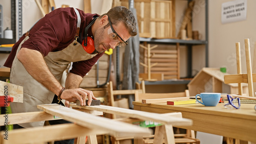 A skilled man measuring wood in a well-equipped carpentry workshop, displaying craftsmanship and focus.