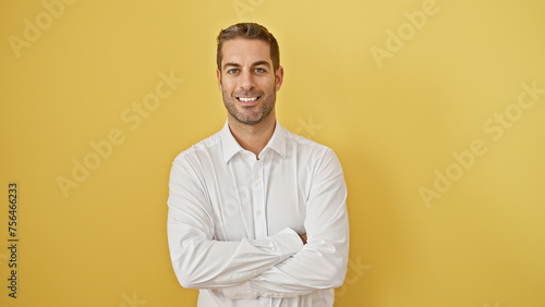 Confident young man with beard in white shirt posing with arms crossed against yellow background, exuding casual professionalism. © Krakenimages.com