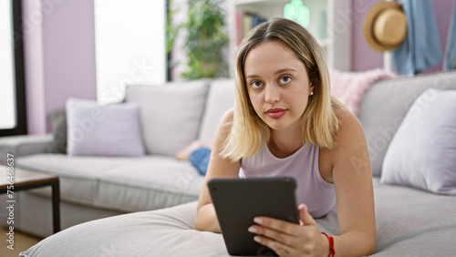 Young blonde woman using touchpad lying on sofa at home