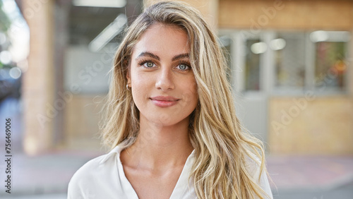 Cool, relaxed young blonde woman seriously looking at camera, standing casually in sunny urban street, attractive lifestyle portrait, outdoors with city background photo