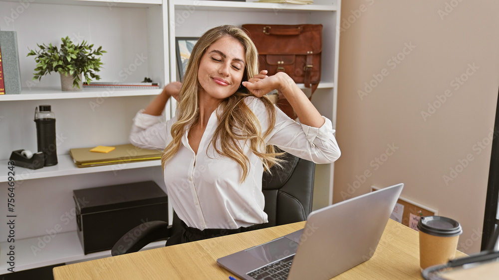 Attractive, confident young blonde businesswoman finds joy in stretching back, taking breather from laptop work at the office - obrazy, fototapety, plakaty 