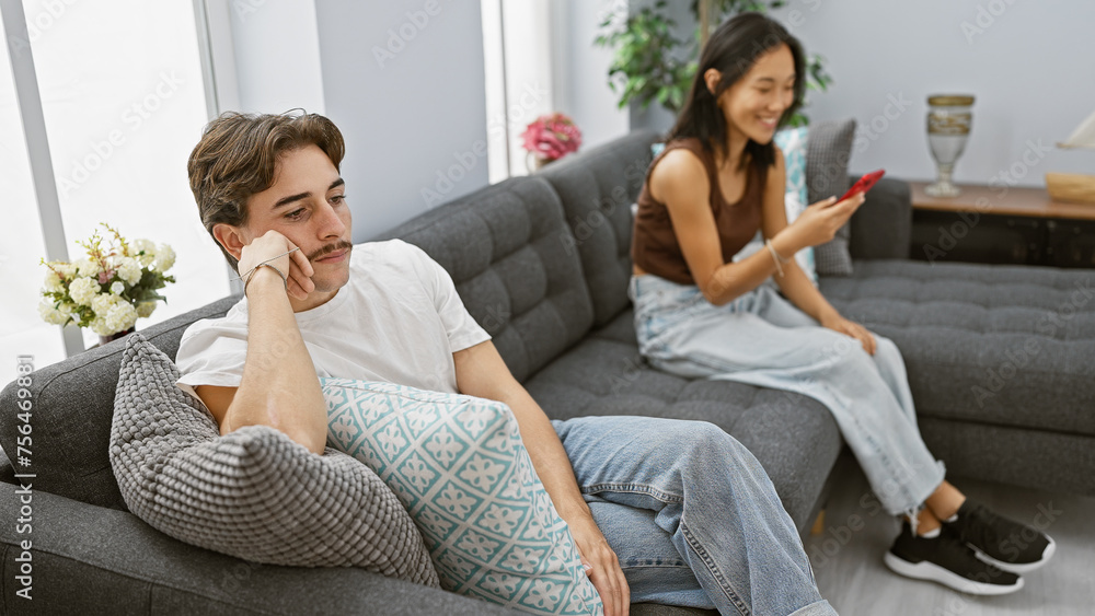 Disinterested man and smiling woman using a smartphone in a modern living room, depicting relationship dynamics. Disinterested man and smiling woman using a smartphone in a modern living room, depicting relationship dynamics.