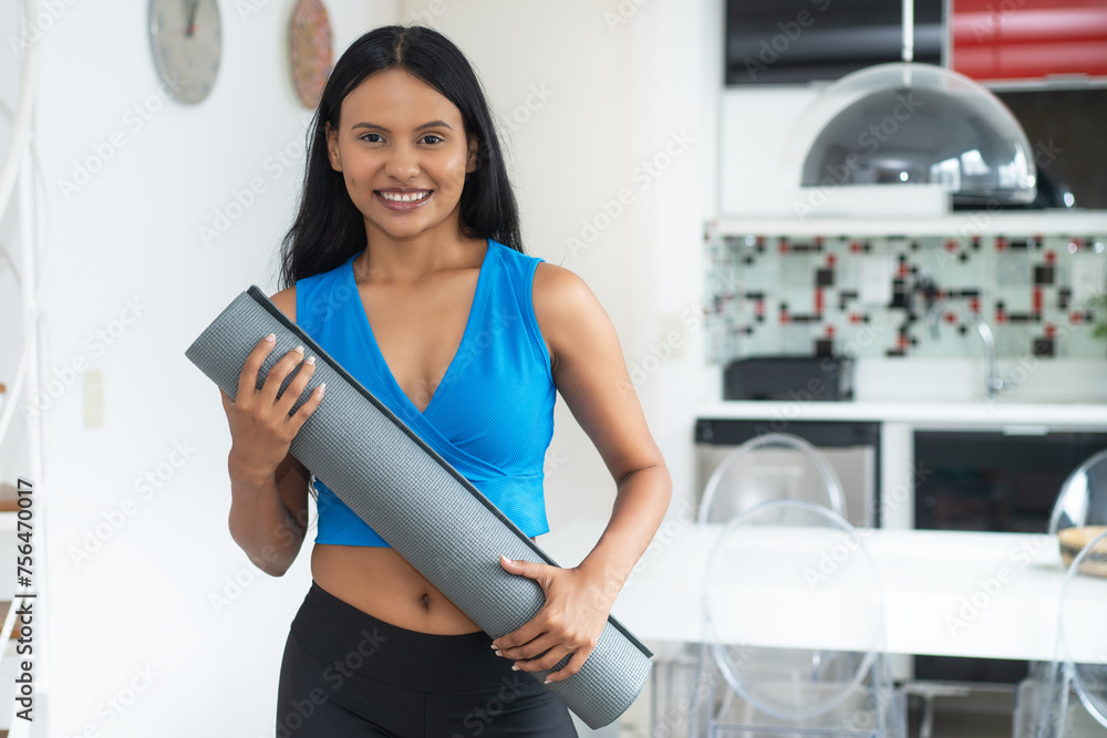 Laughing hispanic woman with yoga mat ready for class at gym - obrazy, fototapety, plakaty 
