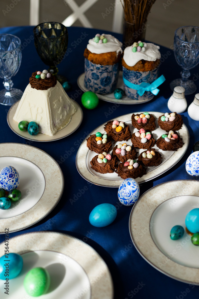 Holiday table laid for Easter celebration with Easter cakes, cookies in shape of nests, tradition cottage cheese Easter and colorful hand-pained Easter eggs