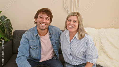 Heartwarming mother and son sitting together on the living room sofa, joyfully hugging and smiling in their cozy home, radiating happiness and confidence in their casual lifestyle.