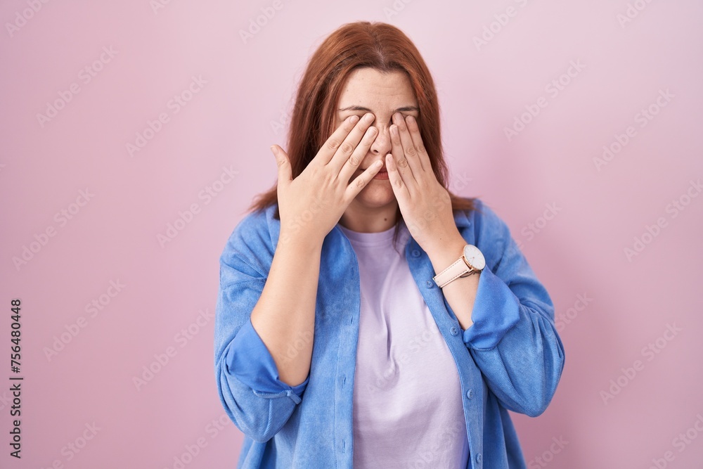 Young hispanic woman with red hair standing over pink background rubbing eyes for fatigue and headache, sleepy and tired expression. vision problem Young hispanic woman with red hair standing over pink background rubbing eyes for fatigue and headache, sleepy and tired expression. vision problem