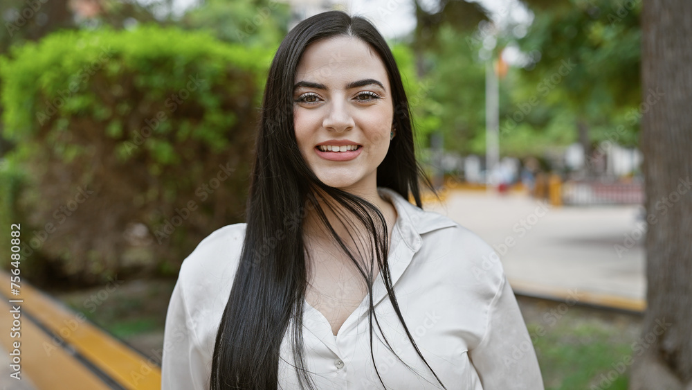 A young hispanic woman with brunette hair smiles in a lush outdoor park. A young hispanic woman with brunette hair smiles in a lush outdoor park.