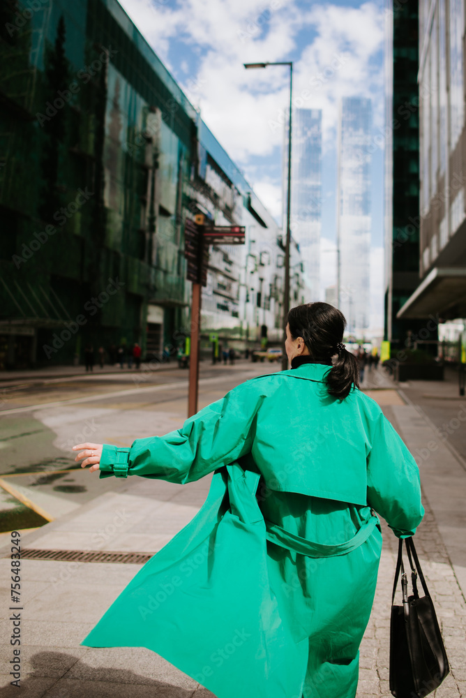 Fototapeta premium woman in a bright green trench coat walks through the city